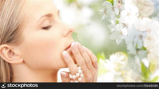 beauty, luxury, people, holidays and jewelry concept - beautiful woman with sea pearls beads in hand over cherry blossom background