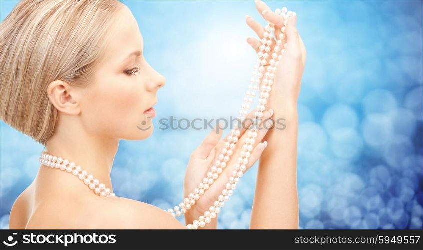 beauty, luxury, people, holidays and jewelry concept - beautiful woman with sea pearl necklace or beads in hands over blue lights background