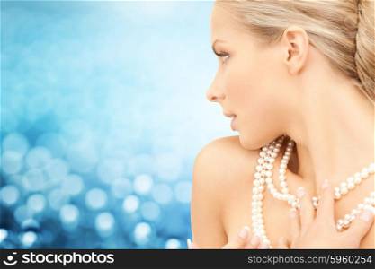 beauty, luxury, people, holidays and jewelry concept - beautiful woman with sea pearl necklace or beads over blue lights background