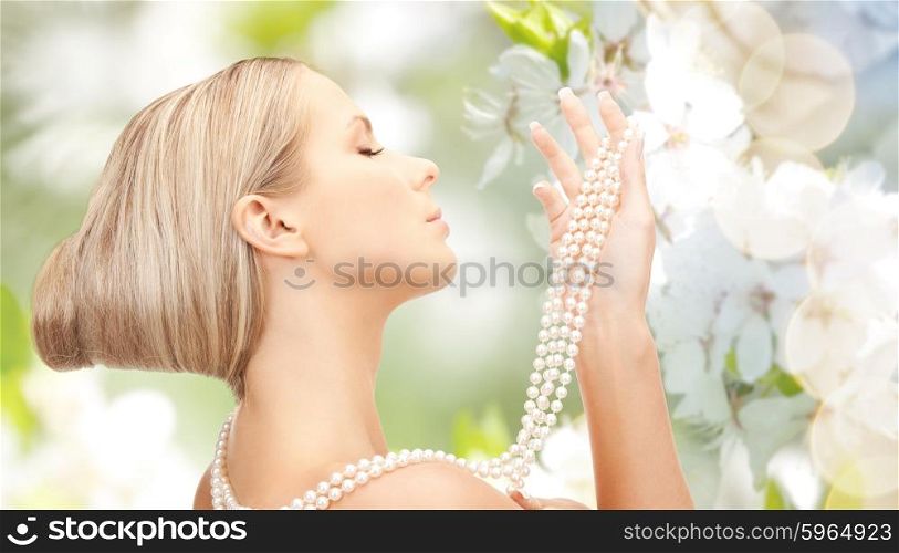 beauty, luxury, people, holidays and jewelry concept - beautiful woman with sea pearl necklace or beads over cherry blossom background