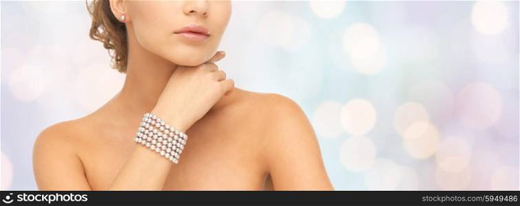 beauty, luxury, people, holidays and jewelry concept - close up of beautiful woman with pearl earrings and bracelet over blue lights background