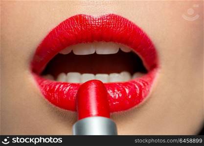 beauty, make up and cosmetics concept - close up of face of woman applying red lipstick to her lips. close up of woman applying red lipstick to lips