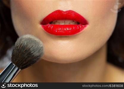 beauty, make up and cosmetics concept - close up of lips or mouth of woman with red lipstick and brush applying face powder to skin. face of woman with red lipstick applying powder