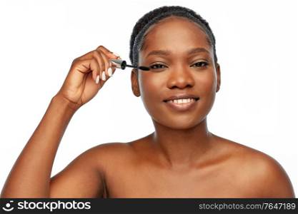 beauty, make up and cosmetics concept - smiling beautiful young african american woman applying mascara over white background. beautiful african american woman applying mascara