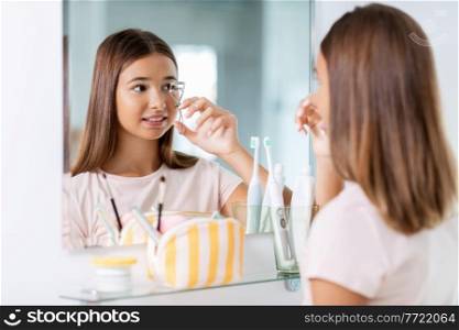 beauty, make up and cosmetics concept - teenage girl curling her lashes and looking to mirror at home bathroom. teenage girl curling her lashes at bathroom
