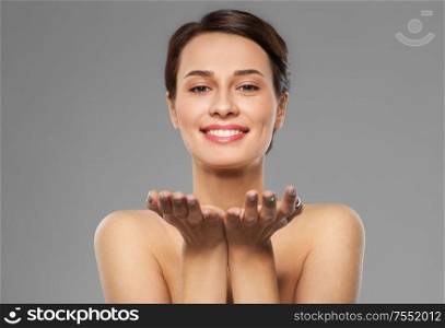 beauty, make up and people concept - happy smiling young woman holding something imaginary on palms over grey background. beautiful young woman holding something on palms