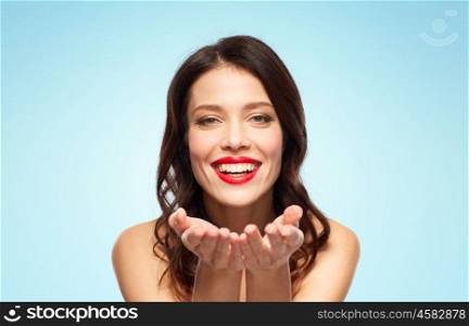 beauty, make up and people concept - happy smiling young woman with red lipstick holding something imaginary on palms over blue background. beautiful smiling young woman with red lipstick. beautiful smiling young woman with red lipstick