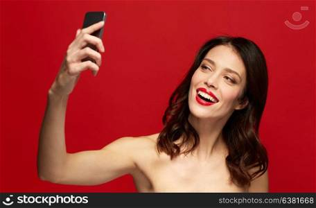 beauty, make up and people concept - happy smiling young woman with red lipstick taking selfie with smartphone. beautiful woman taking selfie with smartphone