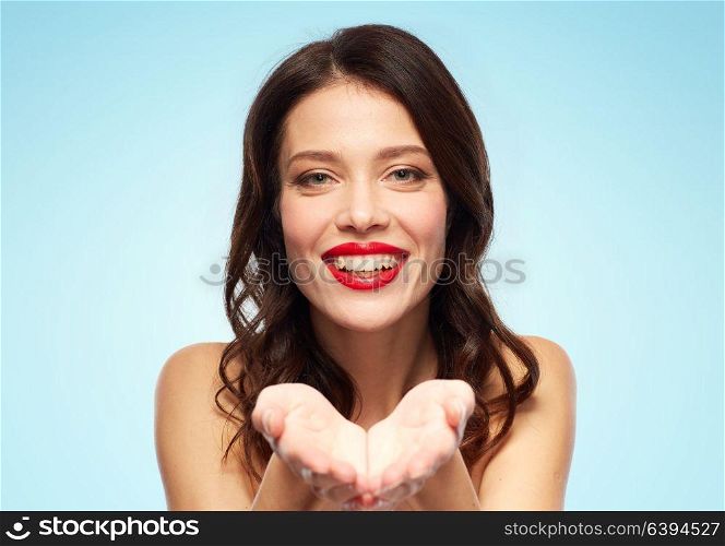 beauty, make up and people concept - happy smiling young woman with red lipstick holding something imaginary on palms over blue background. beautiful smiling young woman with red lipstick