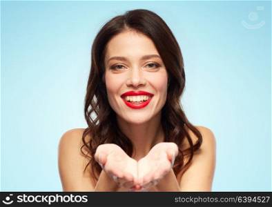 beauty, make up and people concept - happy smiling young woman with red lipstick holding something imaginary on palms over blue background. beautiful smiling young woman with red lipstick