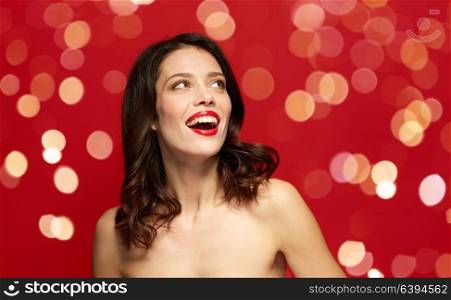 beauty, make up and people concept - happy smiling young woman with red lipstick looking up over red background with lights. beautiful smiling young woman with red lipstick