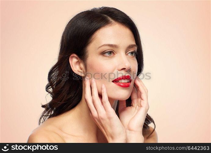 beauty, make up and people concept - happy smiling young woman with red lipstick over beige background touching her face. beautiful smiling young woman with red lipstick