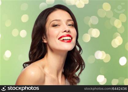beauty, make up and people concept - happy smiling young woman with red lipstick over green background with lights. beautiful smiling young woman with red lipstick