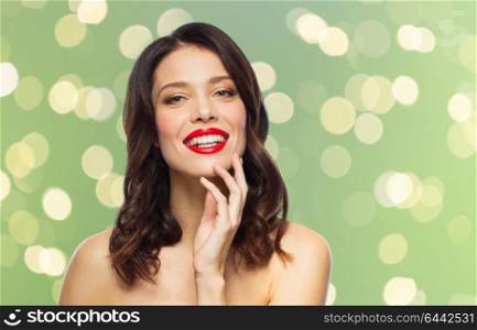 beauty, make up and people concept - happy smiling young woman with red lipstick posing over summer green lights background. beautiful smiling young woman with red lipstick
