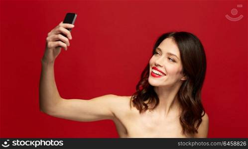 beauty, make up and people concept - happy smiling young woman with red lipstick taking selfie with smartphone. beautiful woman taking selfie with smartphone