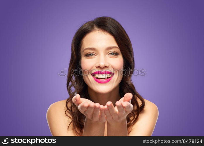 beauty, make up and people concept - happy smiling young woman with pink lipstick holding something imaginary on palms over ultra violet background. beautiful smiling young woman with pink lipstick. beautiful smiling young woman with pink lipstick