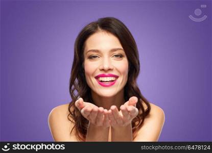 beauty, make up and people concept - happy smiling young woman with pink lipstick holding something imaginary on palms over ultra violet background. beautiful smiling young woman with pink lipstick. beautiful smiling young woman with pink lipstick