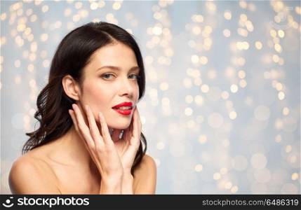 beauty, make up and people concept - happy smiling young woman with red lipstick over holidays lights background touching her face. beautiful smiling young woman with red lipstick. beautiful smiling young woman with red lipstick
