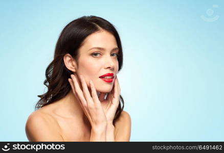 beauty, make up and people concept - happy smiling young woman with red lipstick over blue background touching her face. beautiful smiling young woman with red lipstick. beautiful smiling young woman with red lipstick