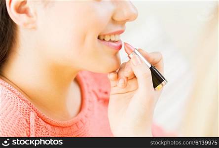 beauty, make up, cosmetics and people concept - close up of smiling young woman face and visagist hand applying lipstick