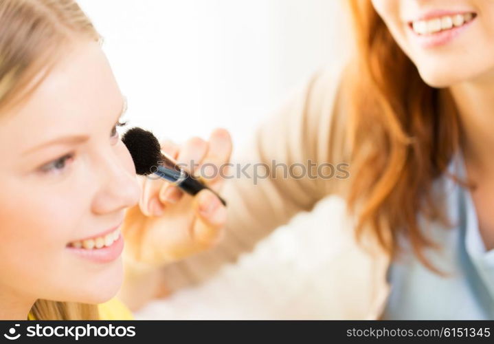 beauty, make up, cosmetics and people concept - close up of smiling young woman and visagist or friend with blush and makeup brush