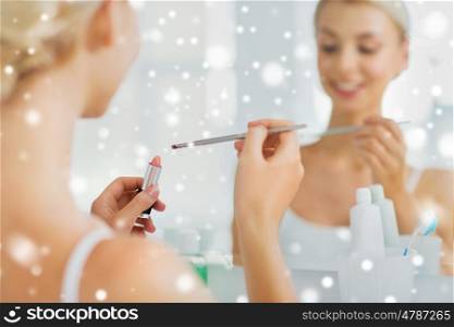 beauty, make up, cosmetics, morning and people concept - close up of smiling young woman with lipstick and brush at home bathroom mirror over snow