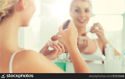 beauty, make up, cosmetics, morning and people concept - close up of young woman makeup brush and powder foundation looking to mirror at home bathroom. woman with makeup brush and powder at bathroom