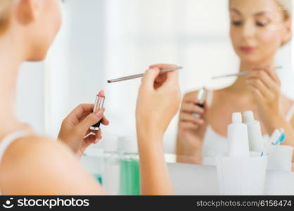 beauty, make up, cosmetics, morning and people concept - close up of young woman with lipstick and make up brush at home bathroom mirror