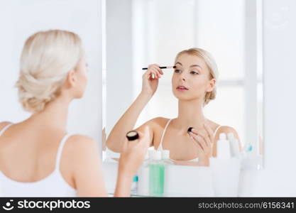 beauty, make up, cosmetics, morning and people concept - young woman applying eyeshade with makeup brush and looking to mirror at home bathroom