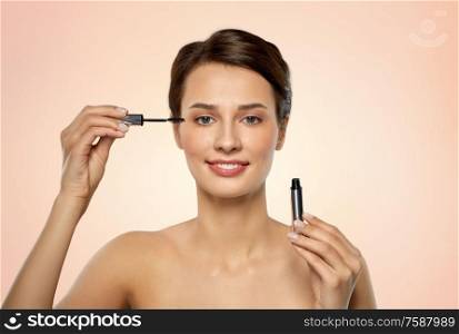 beauty, makeup and cosmetics concept - beautiful young woman applying mascara over beige background. beautiful woman applying mascara