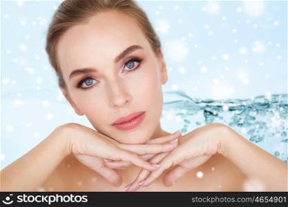 beauty, moisturizing, people and body care concept - close up of beautiful young woman face and hands over water splash bubbles on blue background and snow