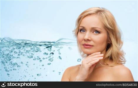 beauty, moisturizing, people and skincare concept - smiling woman with bare shoulders touching face over blue background and water splash