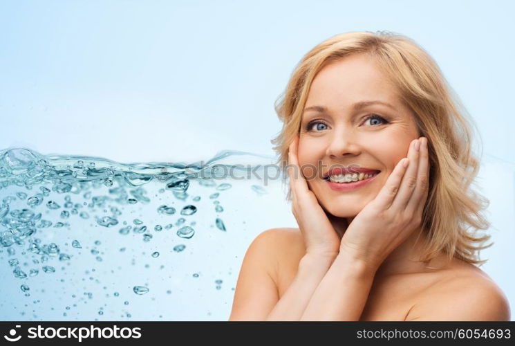 beauty, moisturizing, people and skincare concept - smiling woman with bare shoulders touching face over blue background and water splash