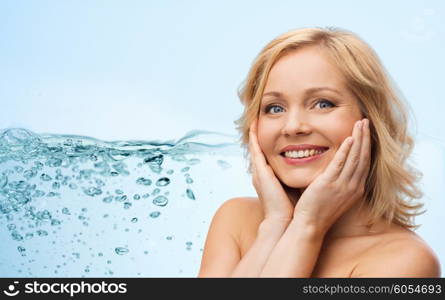 beauty, moisturizing, people and skincare concept - smiling woman with bare shoulders touching face over blue background and water splash