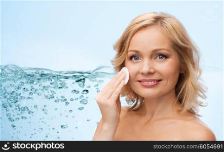 beauty, moisturizing, people and skincare concept - young woman cleaning face and removing make up with cotton pad over blue background and water splash