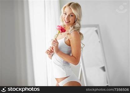 beauty, morning and people concept - beautiful young woman in white underwear smelling peony flower at home window. woman in underwear smelling flower at window