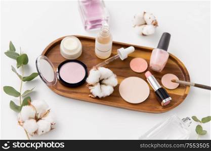 beauty, natural cosmetics and make up products concept - makeup, perfume with cotton flower on wooden tray and eucalyptus cinerea. makeup, perfume and cosmetics on wooden tray