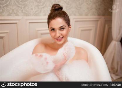 Beauty nude woman playing with foam in bathtub.