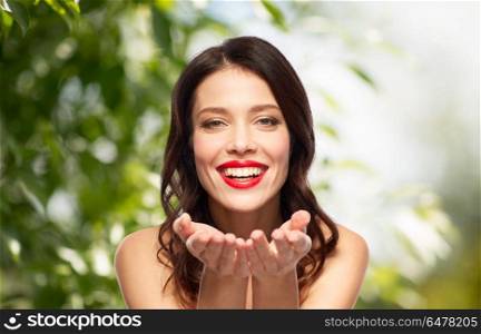 beauty, organic and eco concept - happy smiling young woman with red lipstick holding something imaginary on palms over green natural background. beautiful smiling young woman with red lipstick. beautiful smiling young woman with red lipstick