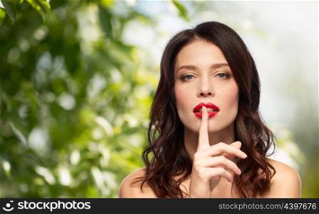 beauty, organic and eco concept - woman holding finger on lips or mouth with red lipstick over green natural background. woman with red lipstick holding finger on mouth. woman with red lipstick holding finger on mouth