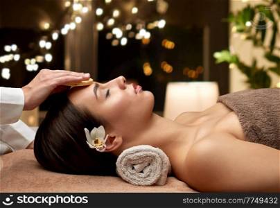 beauty, pampering and relaxation concept - close up of beautiful young woman lying with closed eyes and having face massage with sponge in spa over christmas lights on window background. close up of woman having face massage in spa