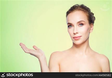 beauty, people, advertisement and health concept - smiling young woman holding something on palm of her hand over green background