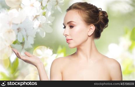 beauty, people, advertisement and health concept - smiling young woman holding something on palm of her hand over natural spring cherry blossom background
