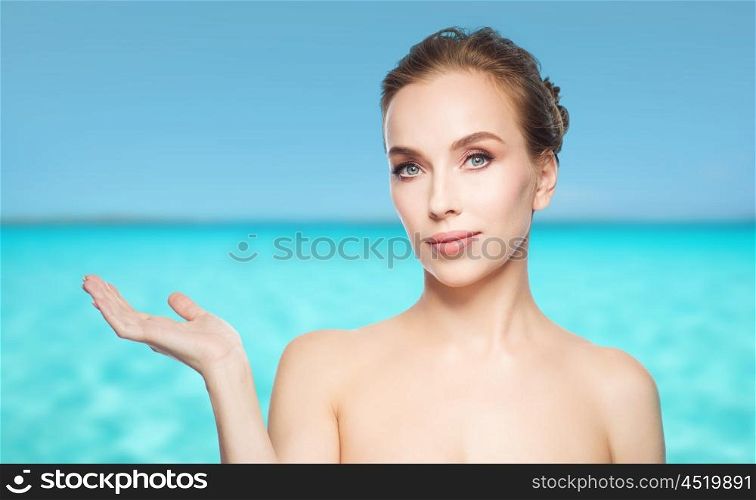beauty, people, advertisement and health concept - smiling young woman holding something on palm of her hand over blue sea and sky background