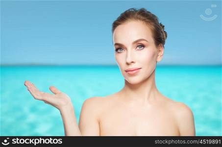 beauty, people, advertisement and health concept - smiling young woman holding something on palm of her hand over blue sea and sky background