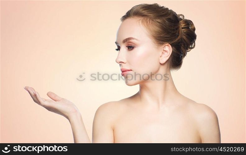 beauty, people, advertisement and health concept - smiling young woman holding something on palm of her hand over beige background