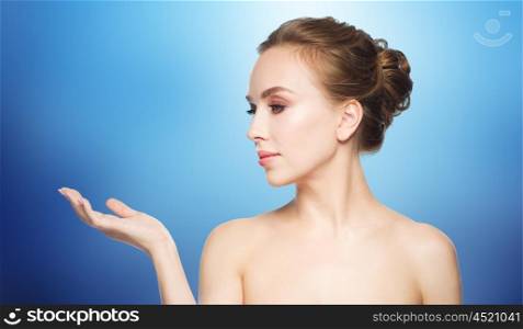 beauty, people, advertisement and health concept - smiling young woman holding something on palm of her hand over blue background