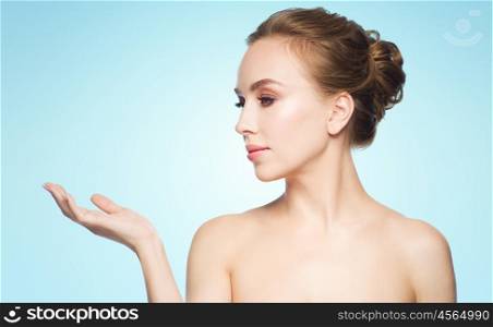beauty, people, advertisement and health concept - smiling young woman holding something on palm of her hand over blue background
