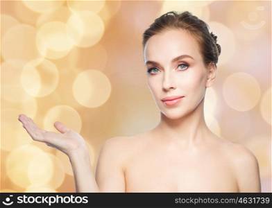 beauty, people, advertisement and health concept - young woman holding something on palm of her hand over holidays lights background