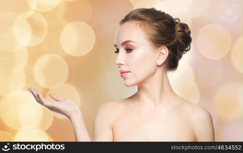 beauty, people, advertisement and health concept - young woman holding something on palm of her hand over holidays lights background